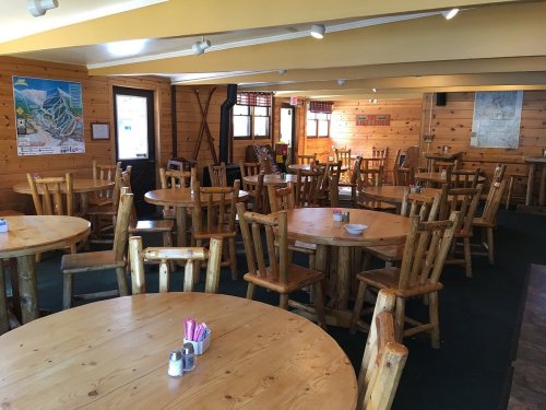 A cozy wooden dining area with round tables and chairs, featuring a warm, rustic atmosphere.