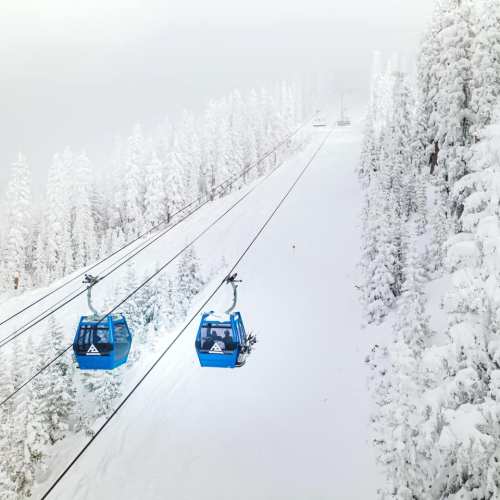 Two blue ski gondolas travel along a snowy cable car line through a winter landscape of frosted trees.