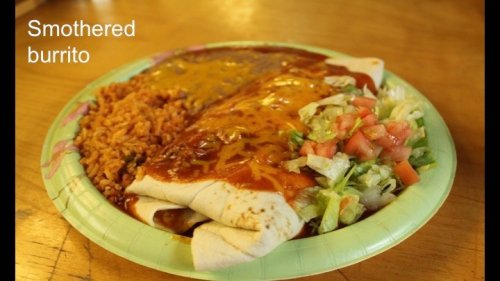 A plate with a smothered burrito, rice, and a side of lettuce and tomato salad.