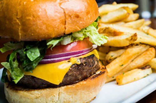 A close-up of a cheeseburger with lettuce, tomato, and onion, served with a side of golden French fries.