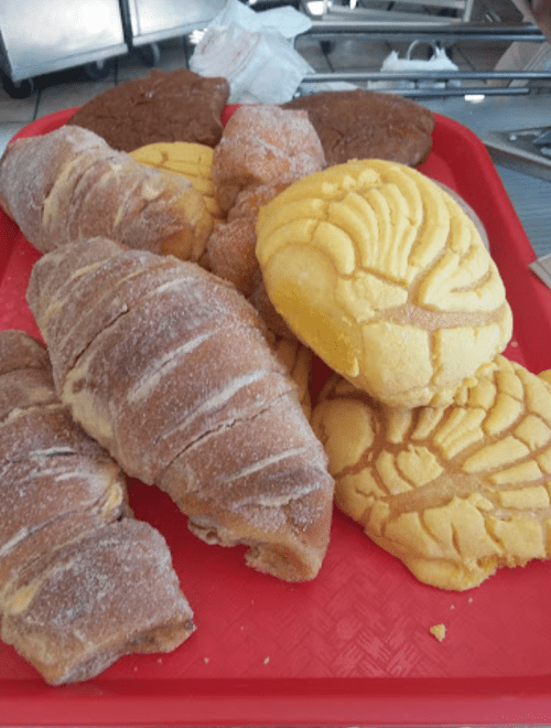A red tray filled with various sweet pastries, including croissants and conchas, showcasing different textures and colors.