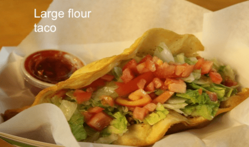 A large flour taco filled with lettuce, tomatoes, and onions, served with a side of salsa.