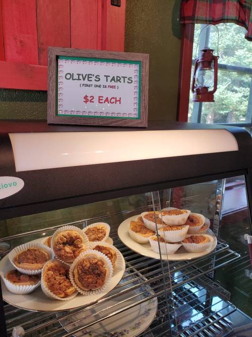 A display case with tarts labeled "Olive's Tarts" for $2 each, with a sign and a rustic background.