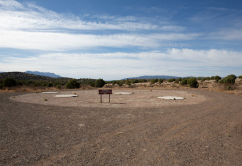 A barren landscape with a circular area marked by two white circles and a sign, under a blue sky with scattered clouds.