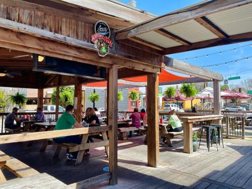 Outdoor dining area with wooden tables, patrons enjoying meals, and hanging plants under a sunny sky.