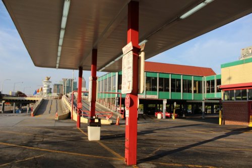 An empty parking area with a covered structure, colorful buildings in the background, and a clear blue sky.