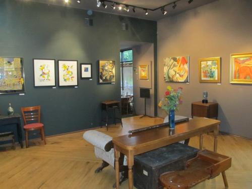 Art gallery interior featuring various paintings, wooden furniture, and a vase of flowers on a table.