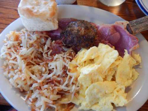 A plate of breakfast featuring scrambled eggs, hash browns, a biscuit, and a sausage patty.