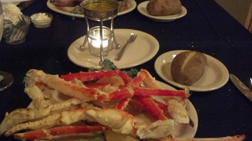 A plate of crab legs with a baked potato and a candle on a table set for dining.