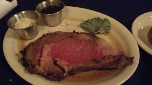 A plate with a large slice of medium-rare prime rib, accompanied by two dipping sauces and a leaf of lettuce.