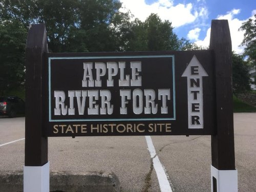 Sign for Apple River Fort State Historic Site, featuring "Enter" arrow and surrounded by trees and blue sky.