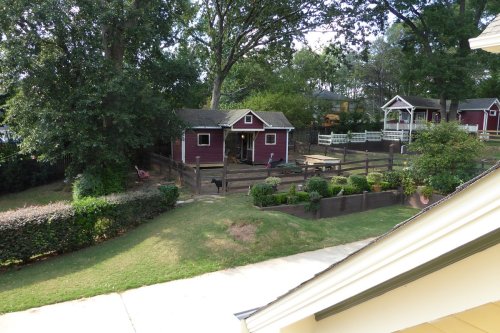 A view of a backyard with a red barn, fenced area, and lush greenery under a clear sky.