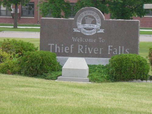 Welcome sign for Thief River Falls, Minnesota, surrounded by greenery and a well-maintained lawn.