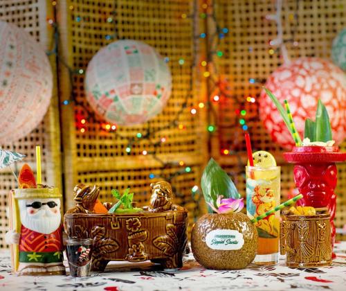 Colorful tiki cocktails in decorative mugs, surrounded by festive lanterns and vibrant decorations.