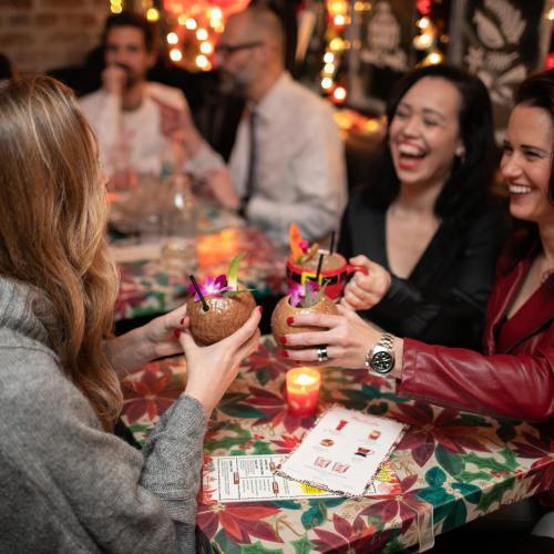 A group of friends toasting with tropical drinks at a festive table, surrounded by warm lights and laughter.