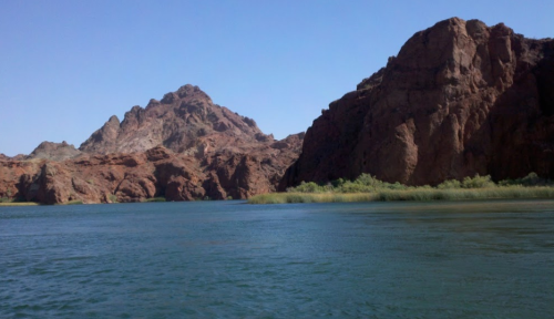 A serene river flows between rocky cliffs and lush greenery under a clear blue sky.