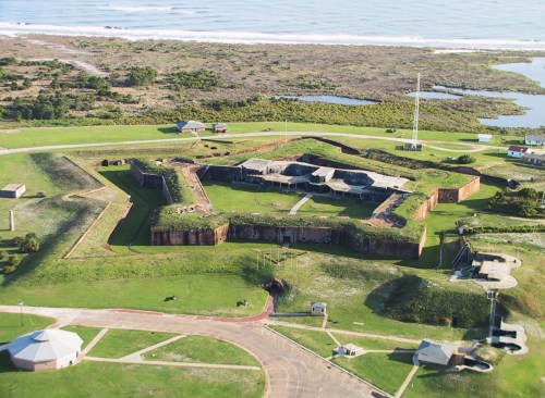 Aerial view of a historic fort surrounded by green fields and near a coastline.