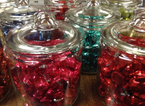 Colorful jars filled with shiny, wrapped candies in red, green, and blue.