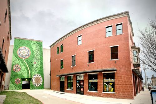 A brick building with large windows, featuring a colorful mural on the side and a curved architectural design.