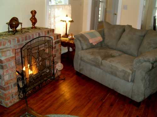 Cozy living room with a brick fireplace, a plush gray couch, and warm lighting from lamps.