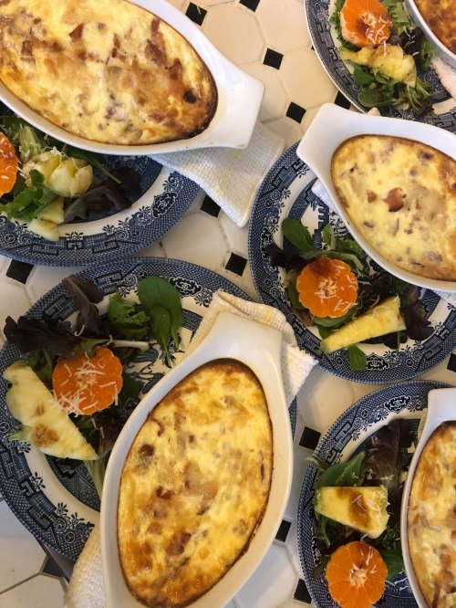 Baked dishes with creamy toppings served on plates with fresh salads and fruit slices.