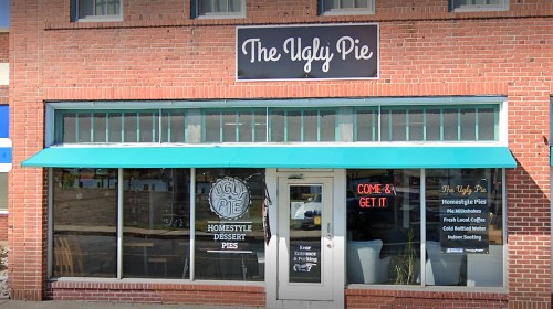 Exterior of "The Ugly Pie" shop featuring a sign, large windows, and an awning, inviting customers to come inside.