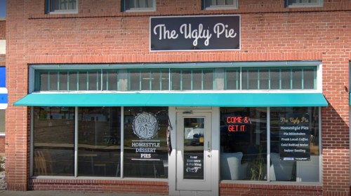Exterior of "The Ugly Pie" bakery with a teal awning, showcasing a sign and window displays of dessert pies.