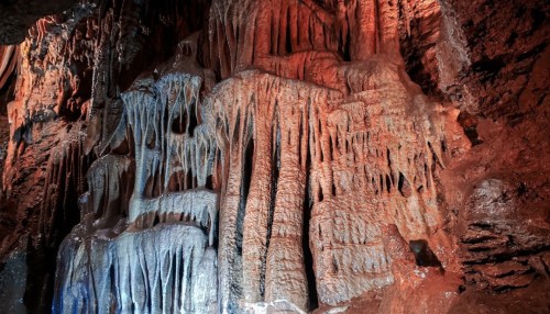 Stalactites and stalagmites in a colorful cave, illuminated with red and blue lighting.