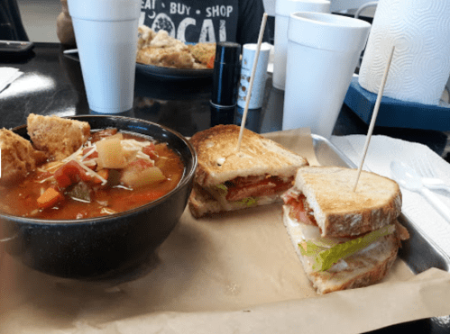 A bowl of vegetable soup next to a toasted sandwich with lettuce, tomato, and turkey, served on a paper tray.