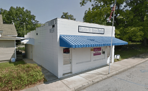 A small white building with a blue awning, labeled "Martin St. Beer Parlor," surrounded by greenery.