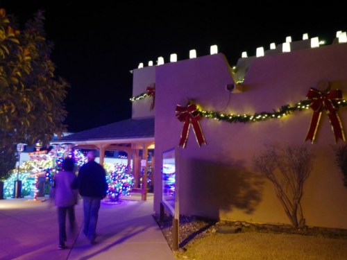 A couple walks past a festively decorated building with Christmas lights and bows at night.