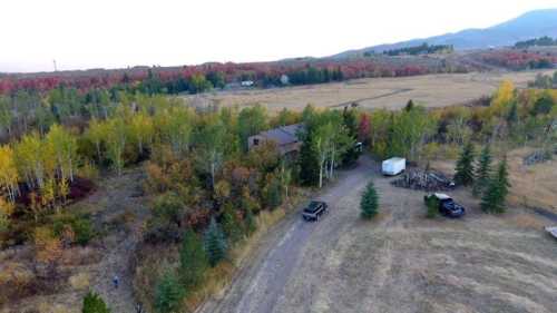 Aerial view of a rural landscape with colorful trees, a house, and parked vehicles on a dirt road.