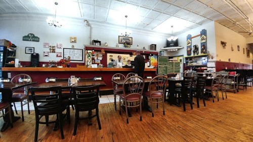 A cozy diner interior with wooden tables, chairs, and a counter where staff serve customers. Decorated with vintage items.