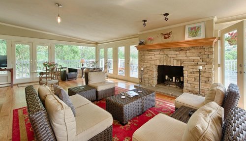 Cozy living room with stone fireplace, wicker furniture, and large windows overlooking a scenic view.