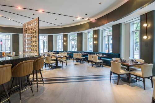 Modern restaurant interior featuring elegant seating, a bar area, and large windows for natural light.