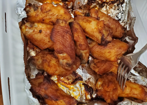 A tray of golden-brown chicken wings, some with a fork resting on them, on a foil-lined surface.