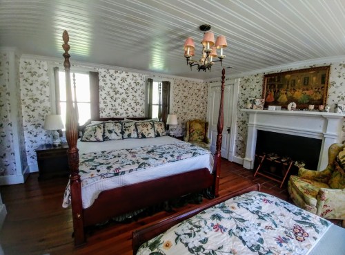 Cozy bedroom with floral wallpaper, two four-poster beds, a fireplace, and vintage decor.