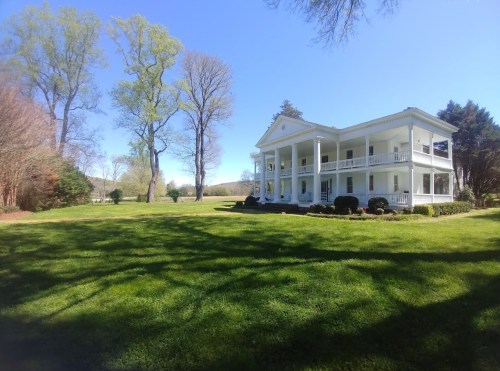 A large white house with columns surrounded by green grass and trees under a clear blue sky.