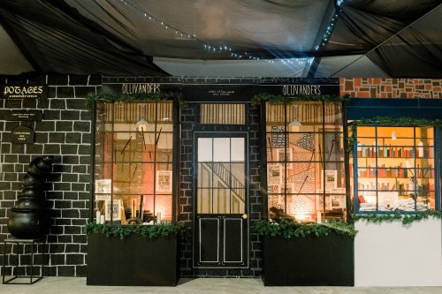 A whimsical storefront resembling Ollivanders wand shop, decorated with greenery and warm lighting.