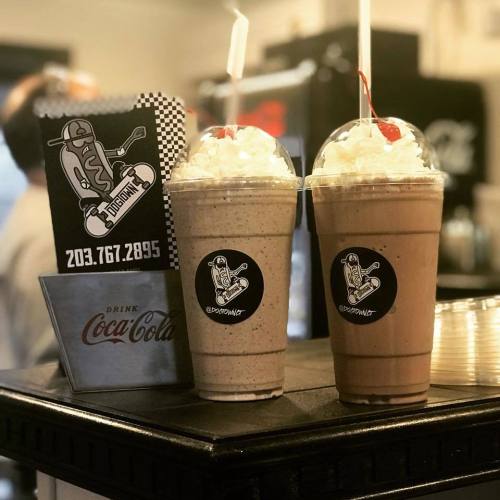 Two milkshakes topped with whipped cream and cherries, placed on a counter next to a Coca-Cola cup.