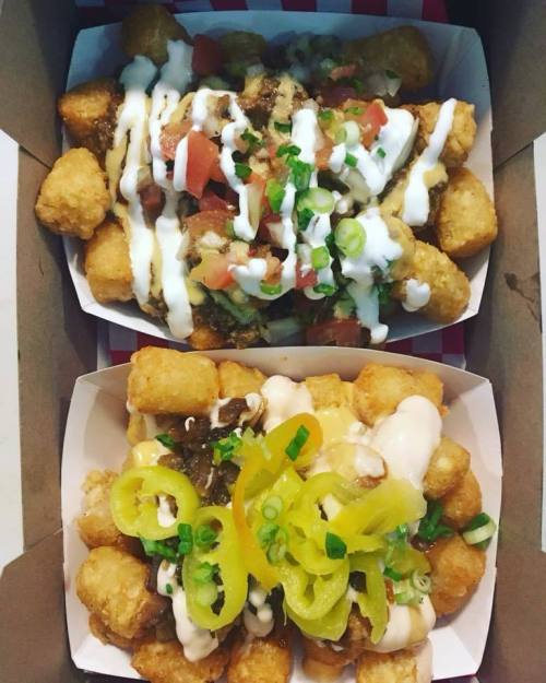 Two boxes of loaded tater tots topped with sauces, tomatoes, green onions, and pickled peppers.
