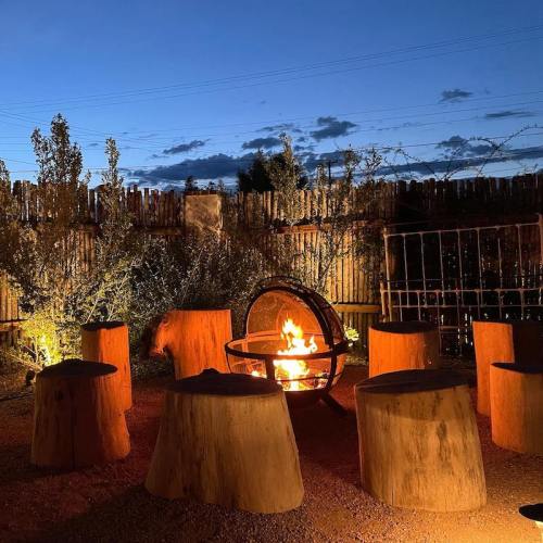 A cozy outdoor seating area with log stools surrounding a fire pit, set against a backdrop of trees and a twilight sky.
