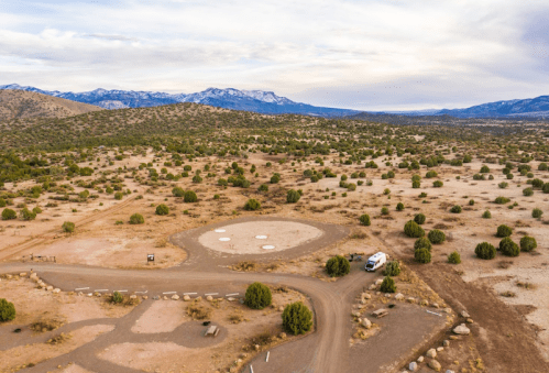Aerial view of a desert landscape with sparse vegetation, a circular area, and a van parked on a dirt road.