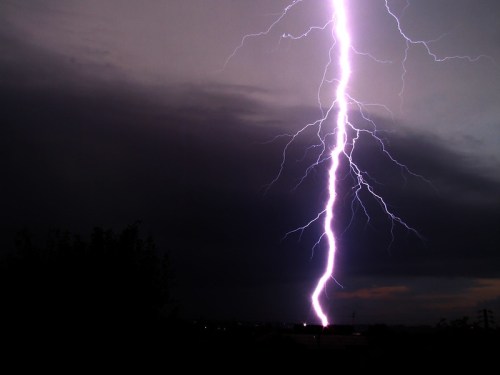 A dramatic lightning bolt strikes down from a dark, stormy sky, illuminating the landscape below.