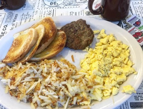 A plate of breakfast featuring toast, a sausage patty, scrambled eggs, and crispy hash browns.
