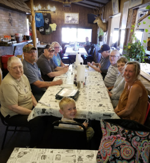 A group of people, including children and adults, sit at a long table in a cozy restaurant.