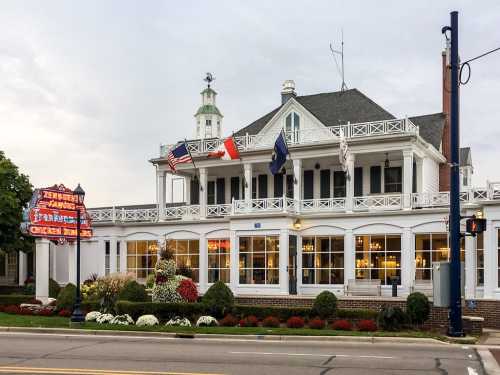 A charming white building with a balcony, flags, and colorful flower beds, serving as a restaurant or inn.