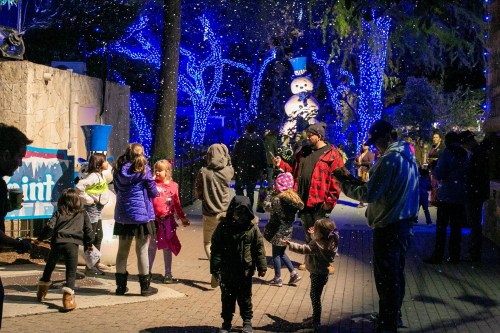 A festive scene with children playing in a snowy area, surrounded by blue lights and a snowman decoration.