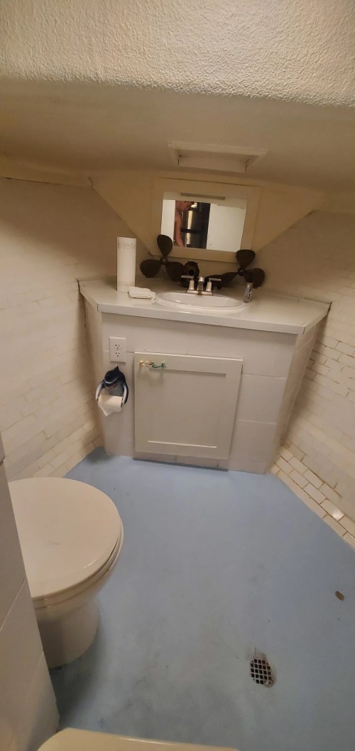 A small bathroom featuring a toilet, sink with a mirror, and tiled walls. The floor is light blue.