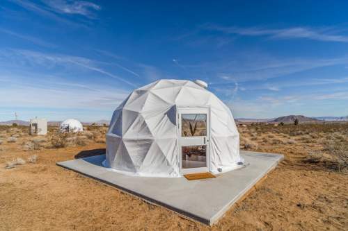 A white geodesic dome on a concrete pad in a desert landscape under a clear blue sky.